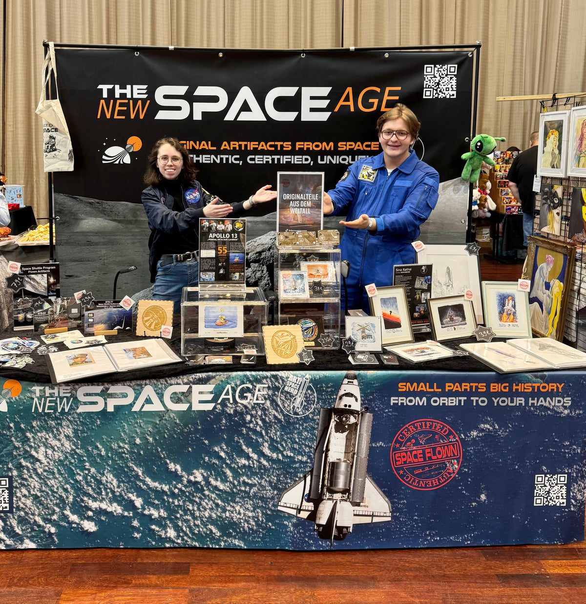 The New Space Age booth at Comic Con Saar 2025 with flown artifacts, framed space art and two team members