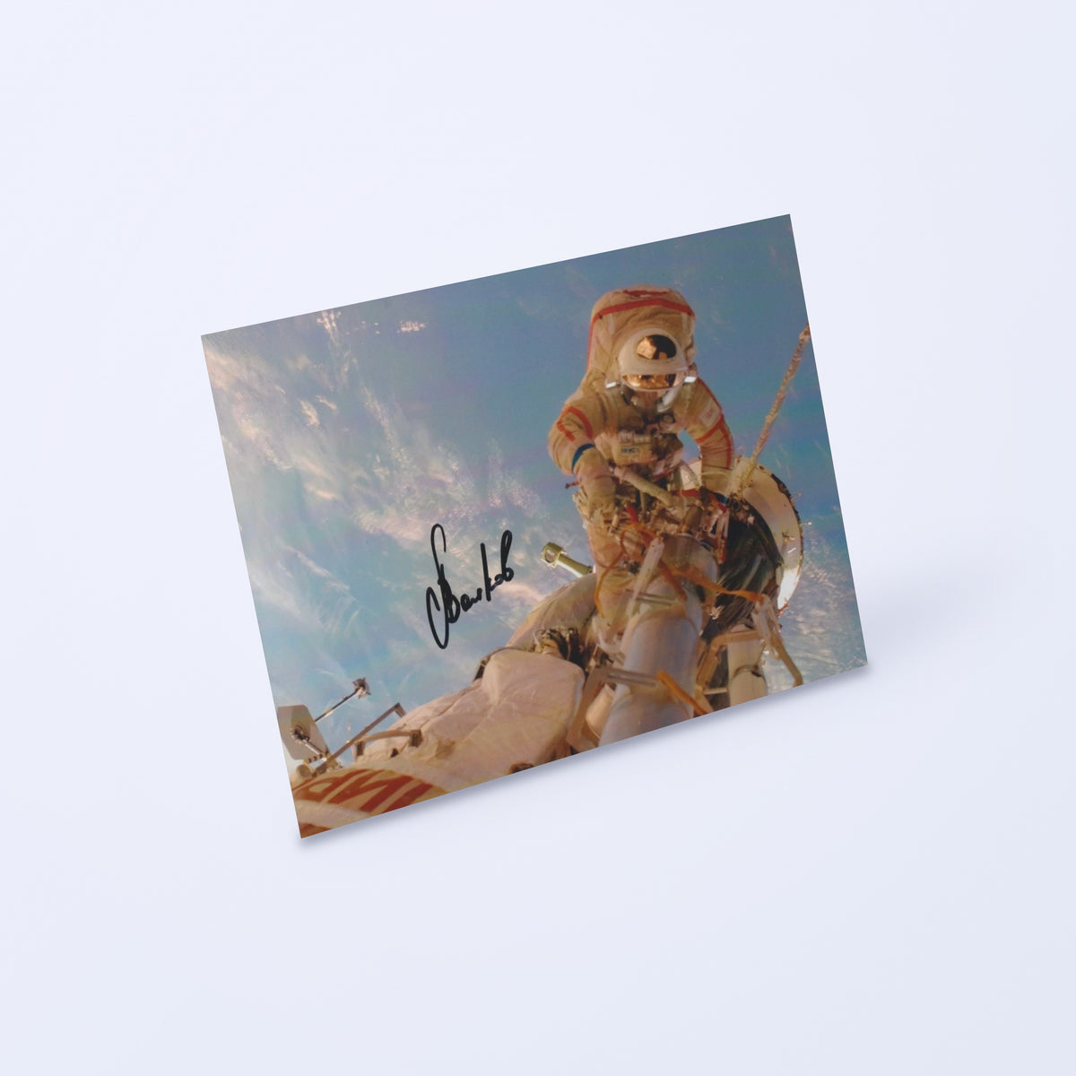 Signed photo of cosmonaut Aleksandr Volkov during a spacewalk above Earth, shown at an angle on a light background