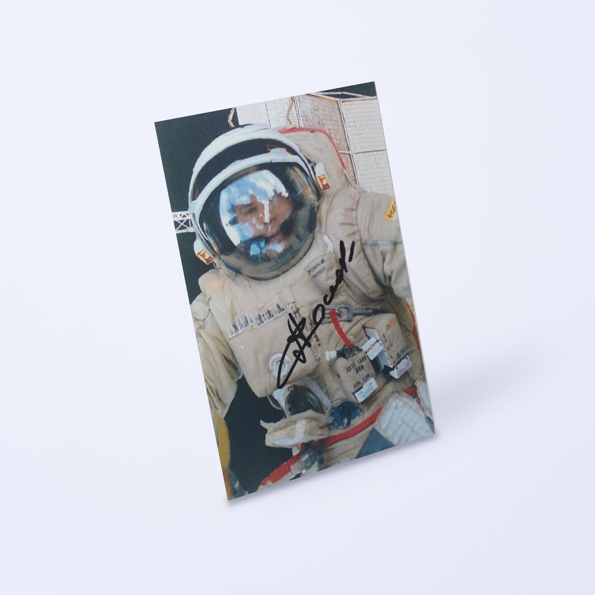 Signed photo of cosmonaut Anatoly Solovyev during a spacewalk, shown at an angle on a light background