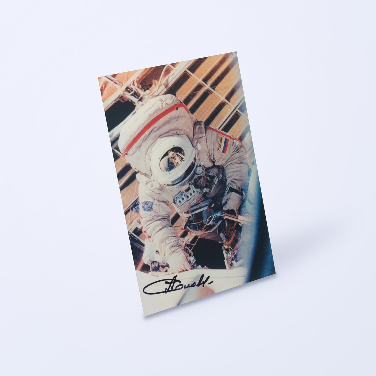 Signed photo of cosmonaut Anatoly Solovyev in an Orlan EVA spacesuit, shown at an angle on a light background