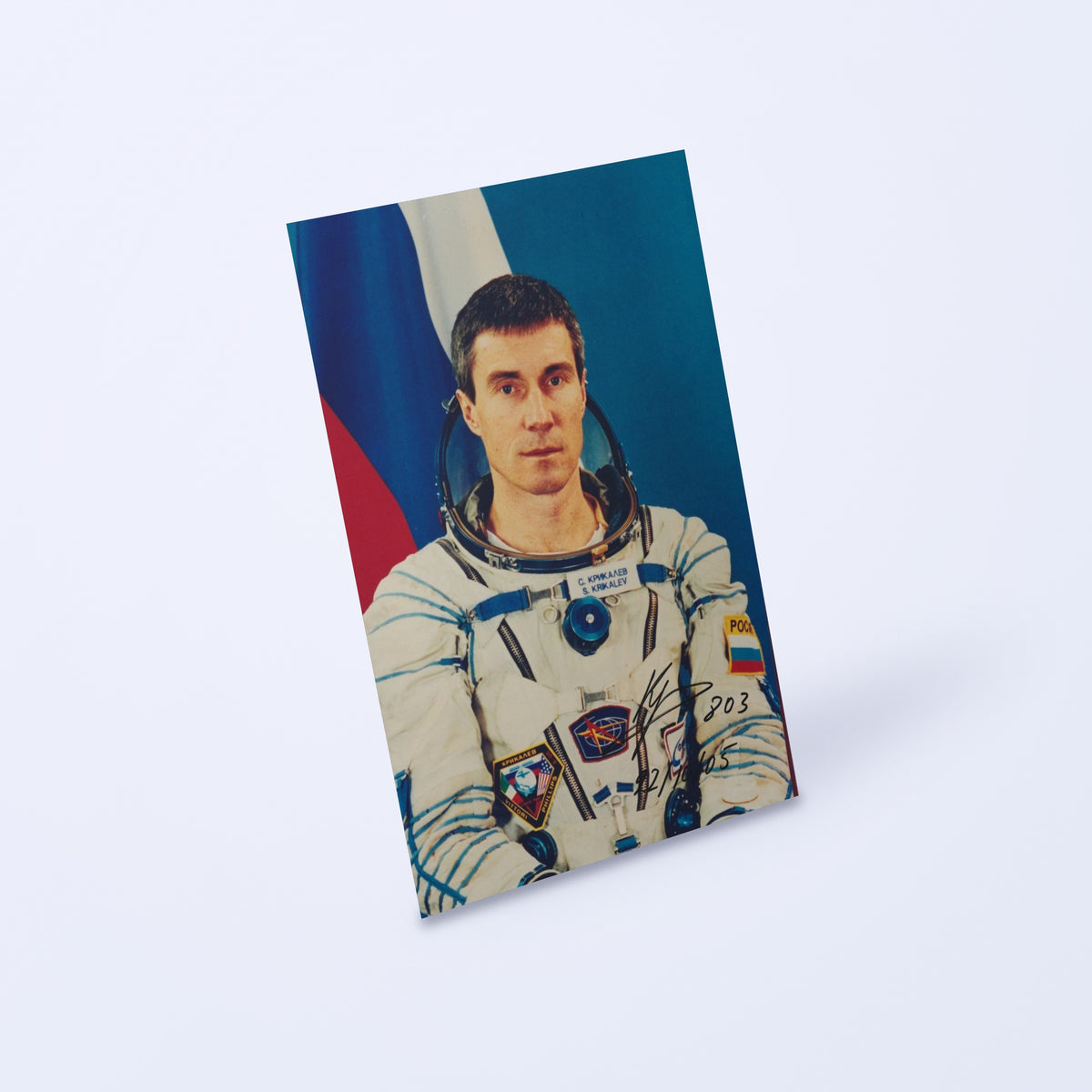 Signed portrait of cosmonaut Sergei Krikalev in a Sokol spacesuit, shown at an angle on a light background