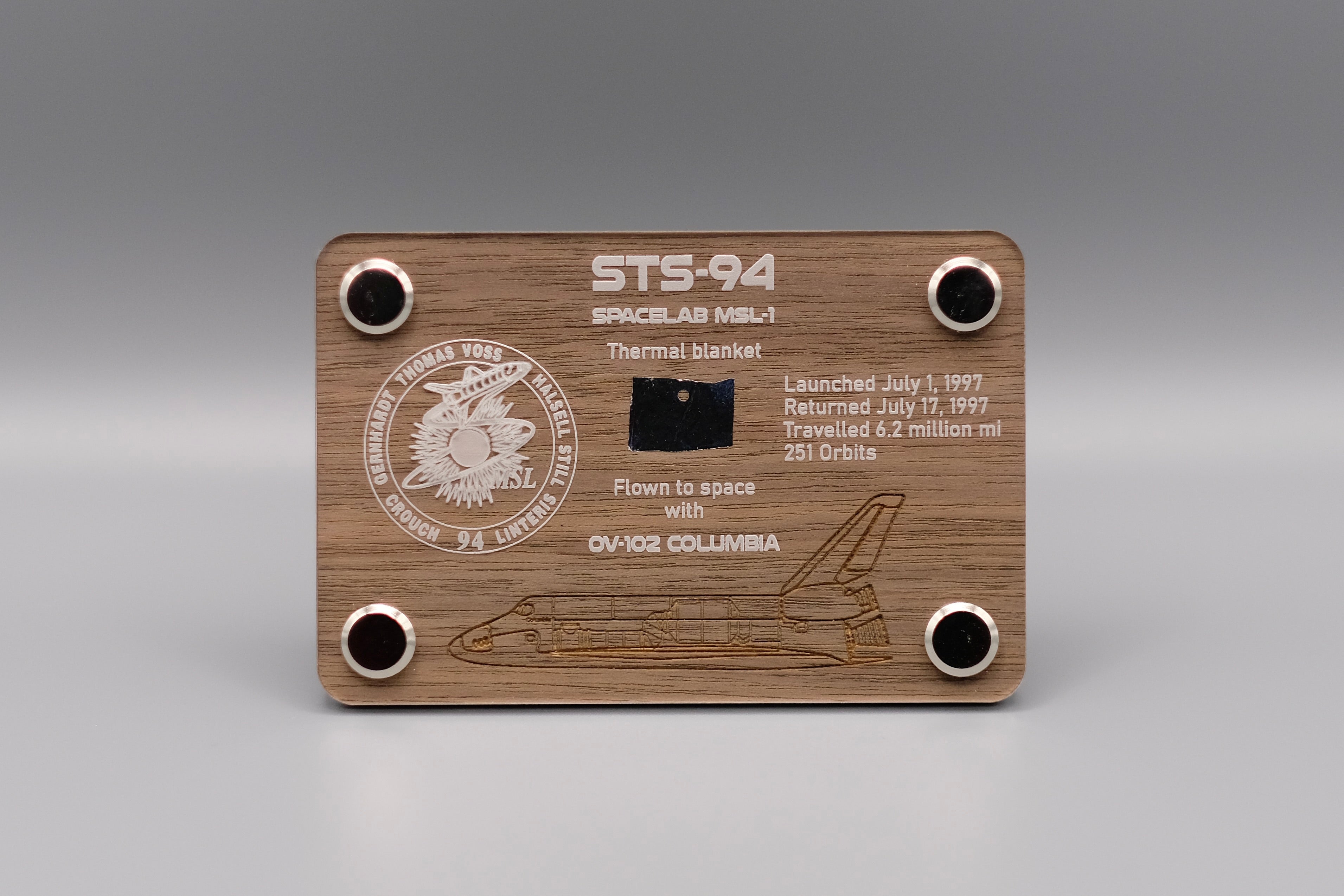 Authentic flown thermal blanket fragment from Space Shuttle Columbia STS-94 (1997) mounted in engraved wooden display with mission patch and shuttle design