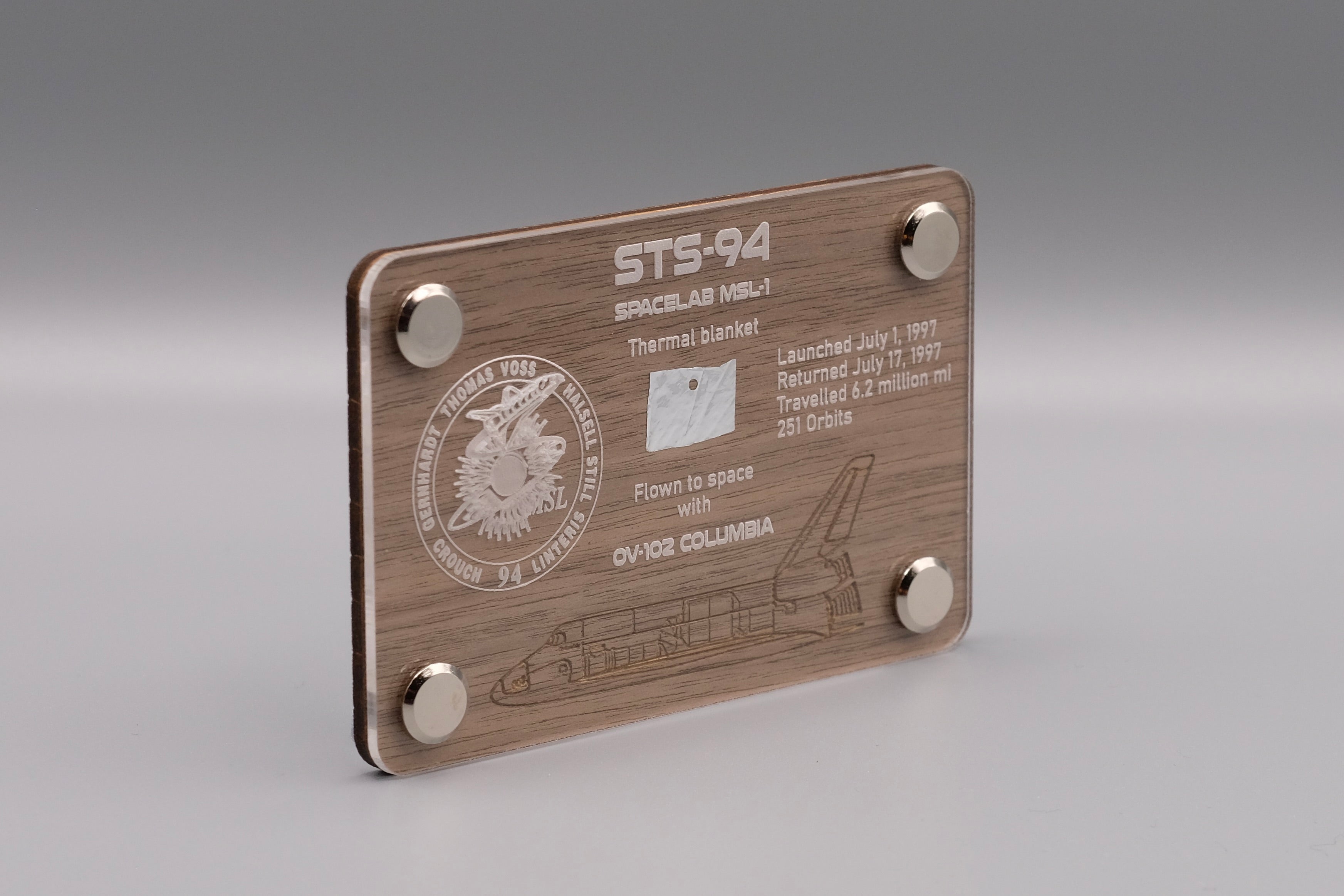 Authentic flown thermal blanket fragment from Space Shuttle Columbia STS-94 (1997) mounted in engraved wooden display with mission patch and shuttle design