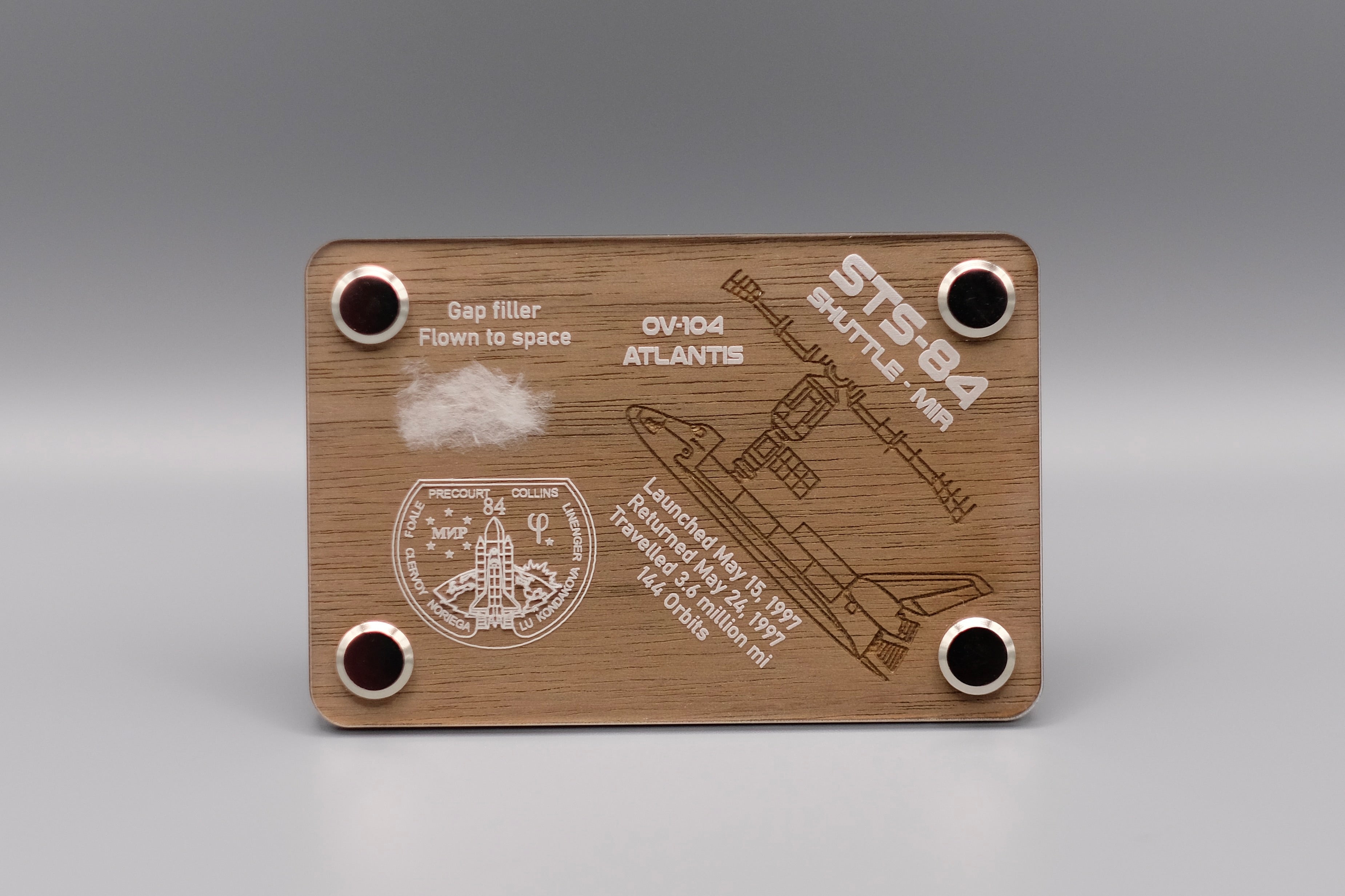 Space Shuttle Atlantis STS-84 display featuring a flown gap filler from the 1997 Shuttle-Mir mission – authentic space-flown artifact mounted on engraved wood plaque, available at The New Space Age Store.