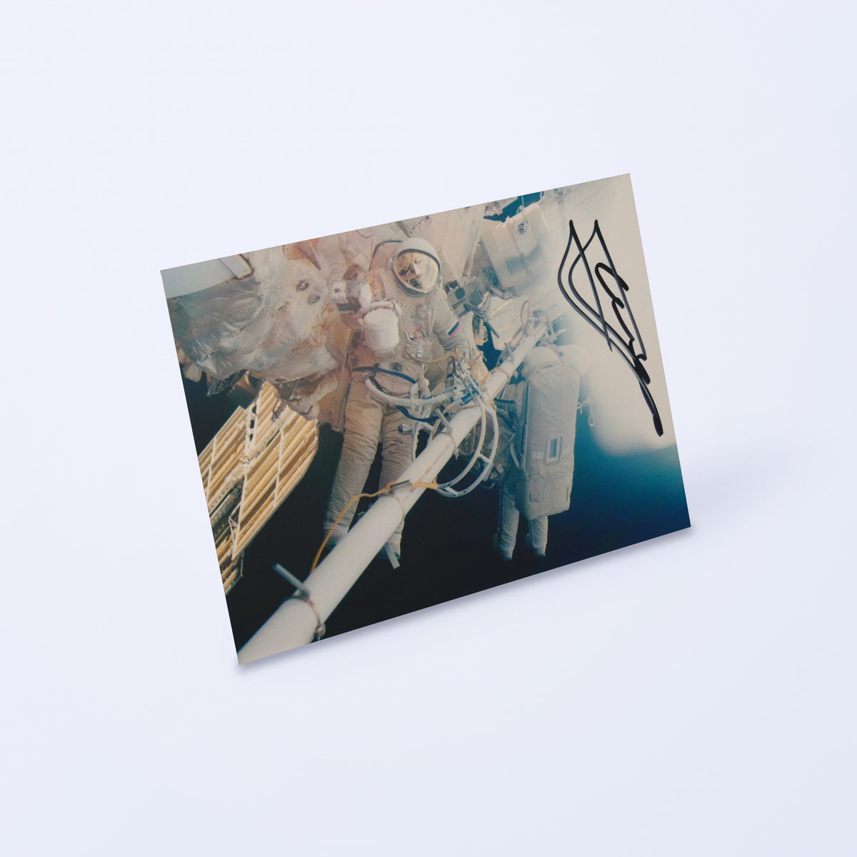 Signed photo of cosmonaut Yuri Gidzenko in an Orlan spacesuit during a spacewalk, shown at an angle on a light background