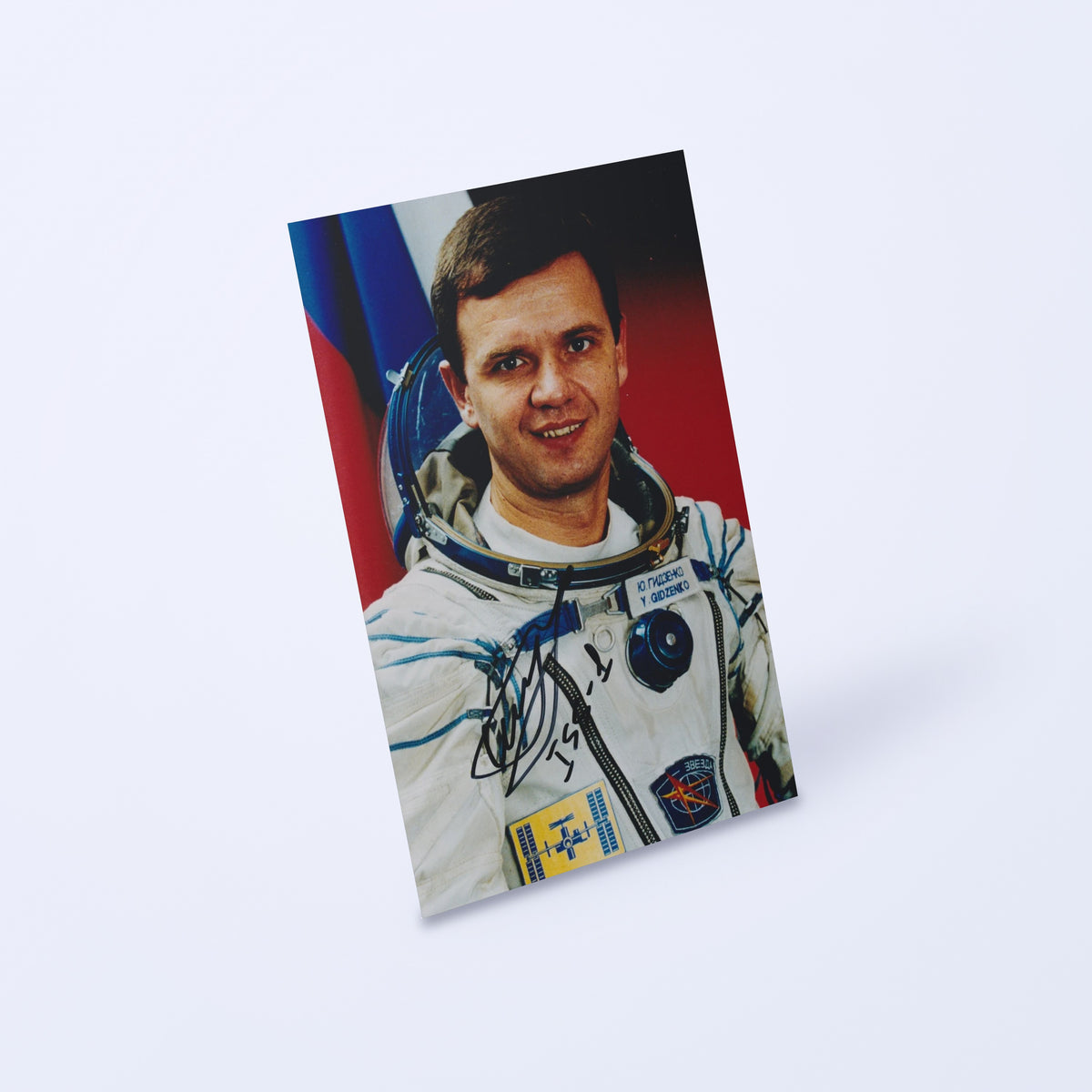 Signed portrait of cosmonaut Yuri Gidzenko in a Sokol spacesuit, shown at an angle on a light background