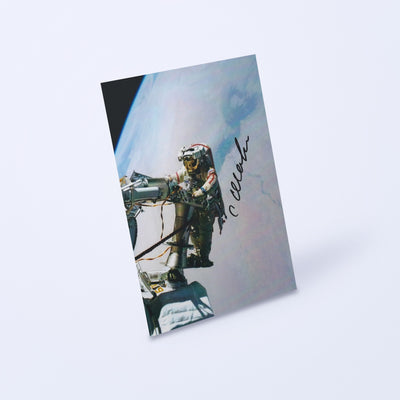 Signed photo of cosmonaut Salizhan Sharipov during a spacewalk above Earth, shown at an angle on a light background