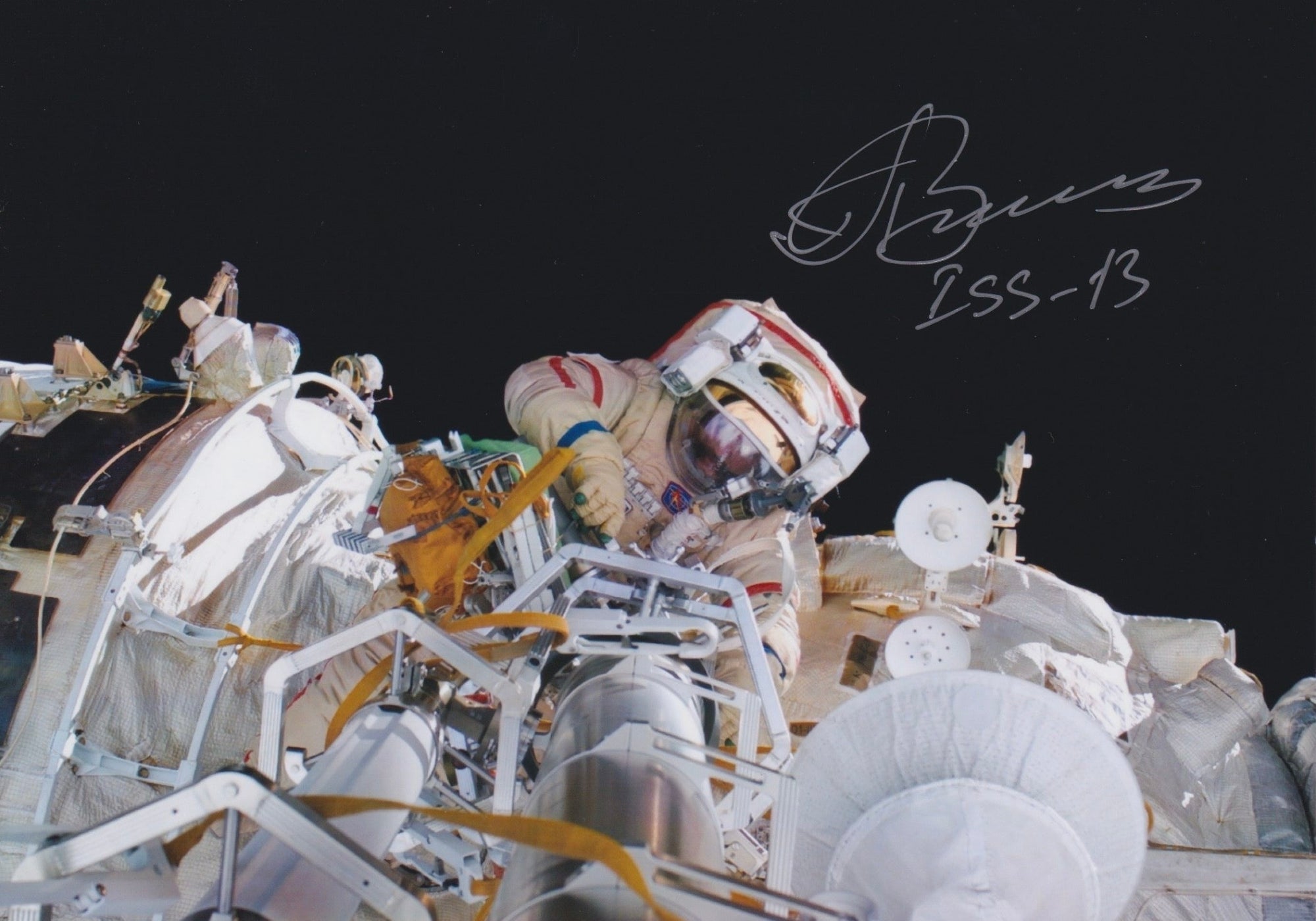 Autographed color photograph of cosmonaut Pavel Vinogradov performing a spacewalk outside the International Space Station during mission ISS-13.