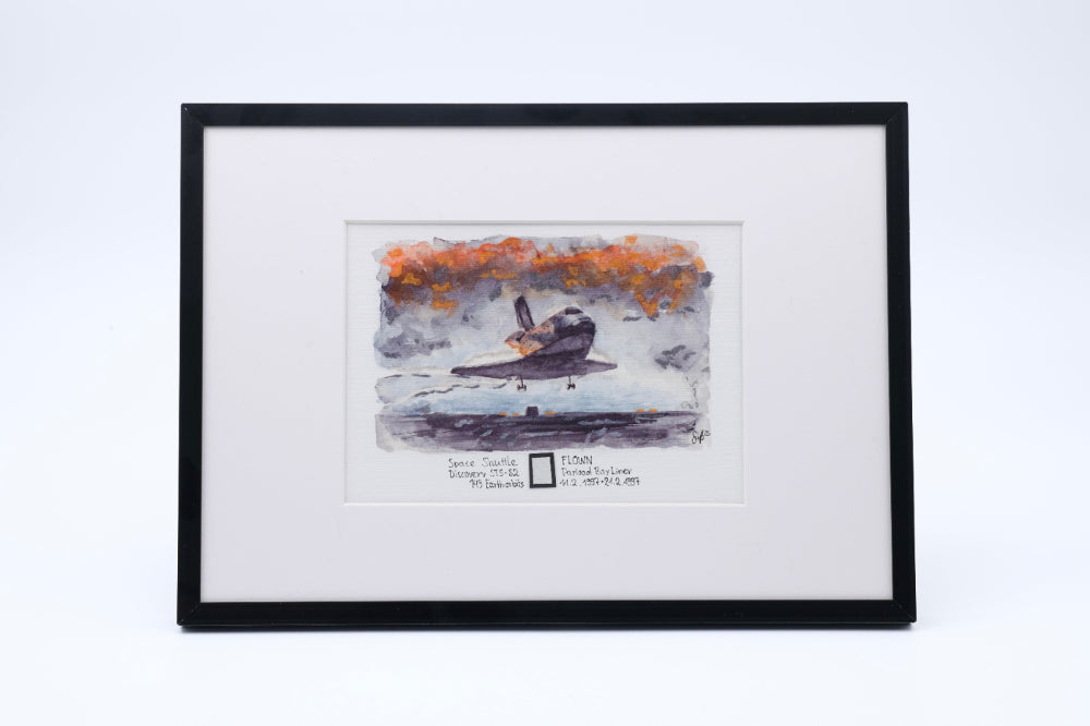 Framed watercolor artwork of Space Shuttle Discovery landing, with a small embedded flown payload bay liner fragment in the print.