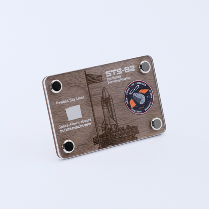 Angled view of an authentic flown payload bay liner artifact display card from Space Shuttle Discovery STS-82, the second Hubble Space Telescope servicing mission.