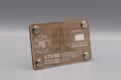 Wooden display with authentic flown Payload Bay Liner fragment from Space Shuttle Discovery STS-82 mission, engraved with Hubble Space Telescope servicing details.