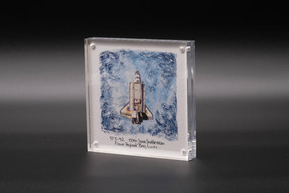 Acrylic display with watercolor artwork of Space Shuttle Discovery and a flown STS-82 payload bay liner fragment inside.