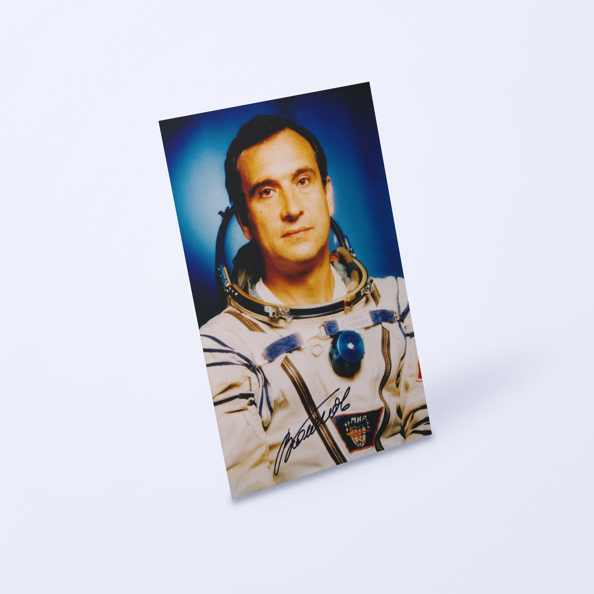 Signed portrait of cosmonaut Valery Polyakov in a Sokol spacesuit with Mir patch, shown at an angle on a light background