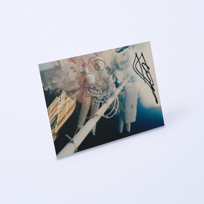 Signed photo of cosmonaut Yuri Gidzenko in an Orlan spacesuit during a spacewalk, shown at an angle on a light background