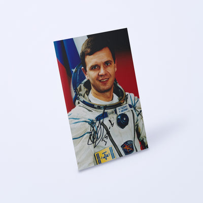 Signed portrait of cosmonaut Yuri Gidzenko in a Sokol spacesuit, shown at an angle on a light background