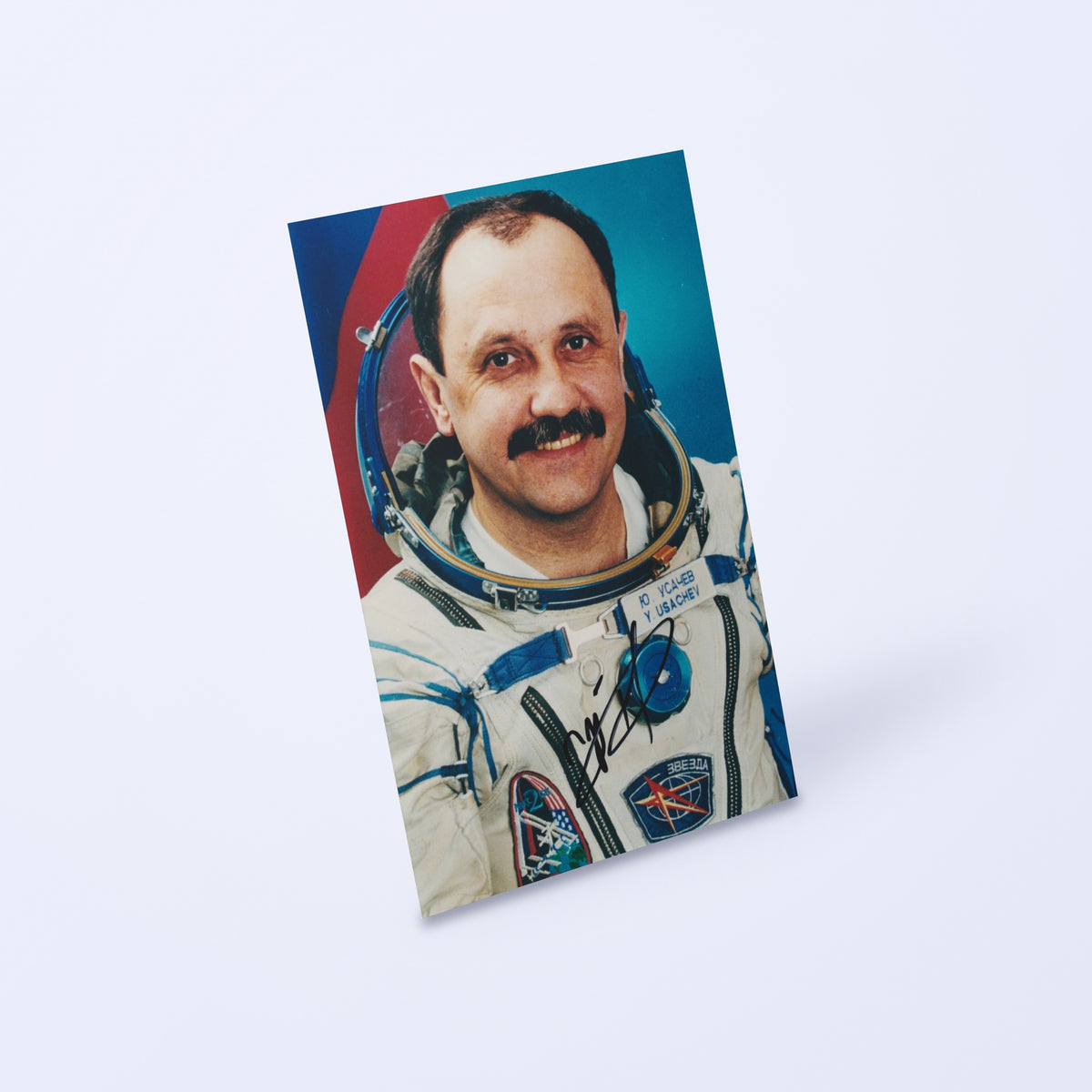 Signed portrait of cosmonaut Yuri Usachev in a Sokol spacesuit, shown at an angle on a light background